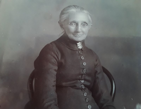 Elderly woman sitting smiling at camera wearing button down dress