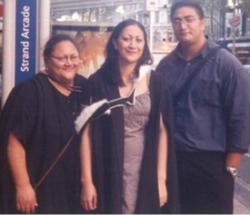 Two women and a man, the middle woman in graduation gown