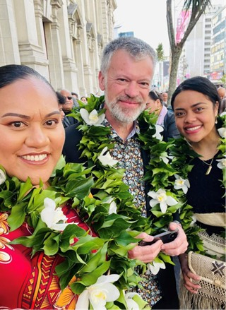Two women each side of man wearing lei and smiling at camera