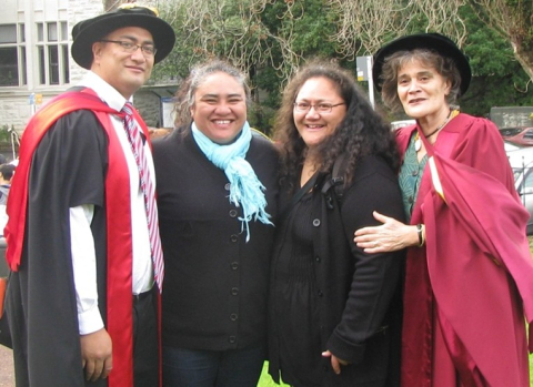 Group of four smiling with outer two in graduation gowns