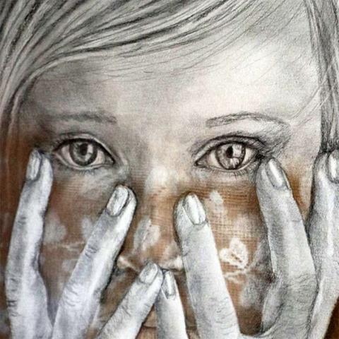 Close up of young woman's face behind her hands held up in protection,