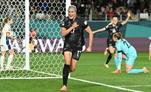 A football player in black uniform runs away from goal with a clenched fist after scoring a goal.