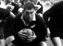 Colin Meads crouched with rugby ball in hand
