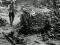 Army medics near a hole surrounded by debris. A solider lies on a stretcher nearby
