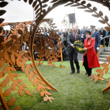 Two people approach steel sculpture holding a wreath of flowers