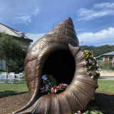 Bronze memorial in the shape of a conch shell covered in flowers