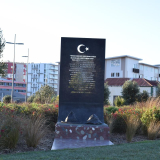 Bronze plaque above reddish-brown polished concrete plinth featuring the shapes of two military hats
