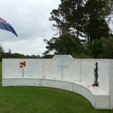 Semi-circular wooden wall with images of red poppies, a cross, and soldier silhouette engraved on it
