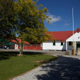 White building with red roof with grass, trees and a flagpole in the foreground