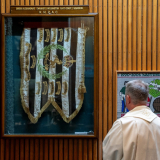 Person in religious robes looking at flag encased in glass fixed to wood-paneled wall. 