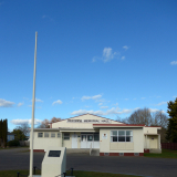 Flagpole and stone plinth in front of red and white building.