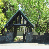 Large wooden lychgate and stone wall with leafy trees behind