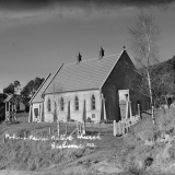 Greyscale photograph of church in a rural setting with bush in the background