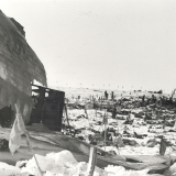 Wreckage of part of airplane fuselage with debris scattered over ice. Flags dot the landscape