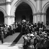 Crowd gathered on steps of parliament around a man holding up a scroll of paper