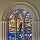 Stained-glass window with figure point to sky and words 'In the wings of the morning' along the bottom