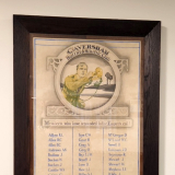 Three columns of names underneath picture of soldier with bugle inside glass frame.