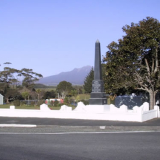 Stone obelisk with buildings, trees and mountain in the background