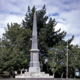 Stone obelisk set on lawn against stand of trees