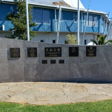 Concrete wall with bronze plaques attached and curve mosaic pattern at either end