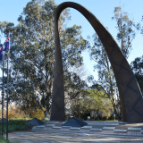 Handle-shaped bronze memorial set into concrete behind two flags and flagpoles.