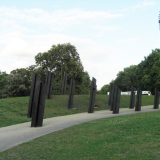 Group of bronze standards sticking out of grass and concrete in a park.