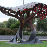 Stylised metal sculpture of two trees. A floral wreath sits in the roots.