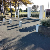 Side view of iron gates between two white pillars and interpretation boards with text. A grass field and trees are in the background.