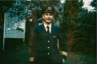 Man in blue pilot's uniform and hat smiling at camera