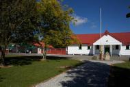 White building with red roof with grass, trees and a flagpole in the foreground