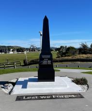 Black granite obelisk set into concrete inlaid with the words Lest we Forget