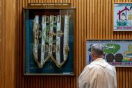 Person in religious robes looking at flag encased in glass fixed to wood-paneled wall. 
