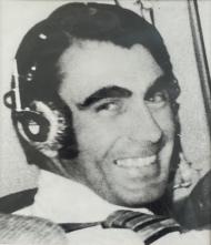 Pilot in cockpit of aircraft with ear phones on smiling at the camera
