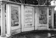 Marble stone memorial consisting of a central panel of text flanked by reliefs of human figures.
