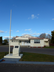 Flagpole and stone plinth in front of red and white building.