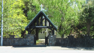 Large wooden lychgate and stone wall with leafy trees behind
