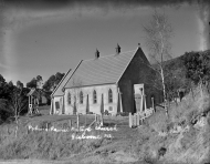 Greyscale photograph of church in a rural setting with bush in the background