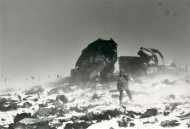 Man standing in snow blizzard surrounded by plan wreckage