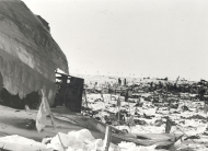 Wreckage of part of airplane fuselage with debris scattered over ice. Flags dot the landscape