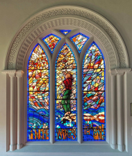 Stained-glass window with figure point to sky and words 'In the wings of the morning' along the bottom