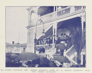 Historic image with crowd gathered on deck and grounds of two-storey wooden building with a lamp in front. One person is speaking to the crowdd