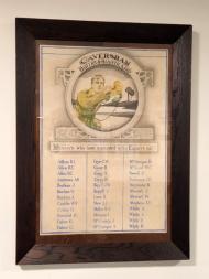 Three columns of names underneath picture of soldier with bugle inside glass frame.
