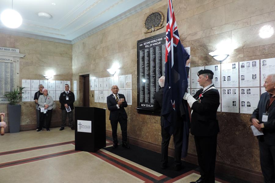 Group of people standing behind lectern in front of black plaque with list of names 