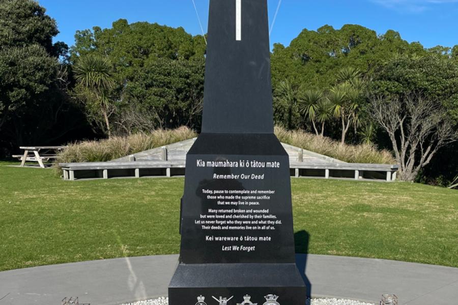 Black granite obelisk set into grass with trees and flagpole in the background