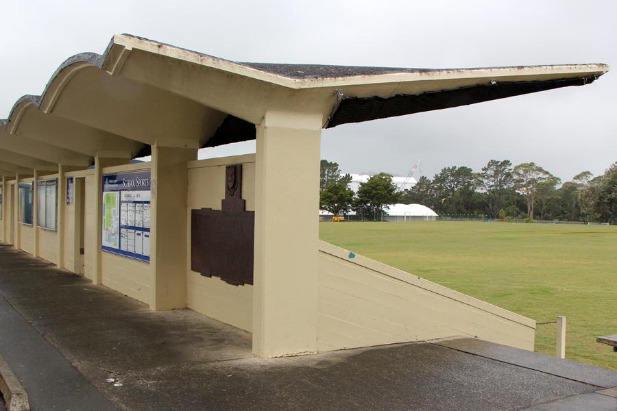 Brass plaque fixed to the rear wall of sports grandstand with grass playing field in the background