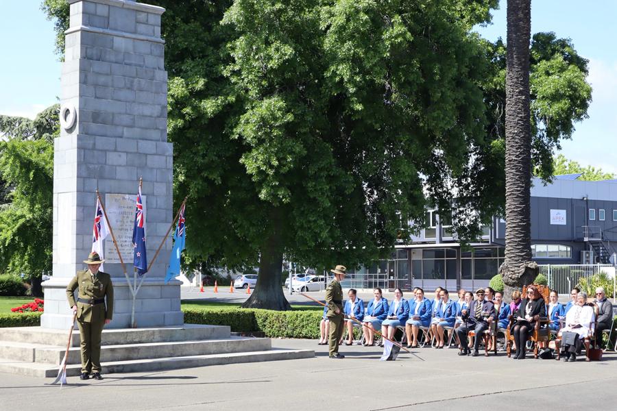 Group of people sitting in seats next to concrete cenotaph
