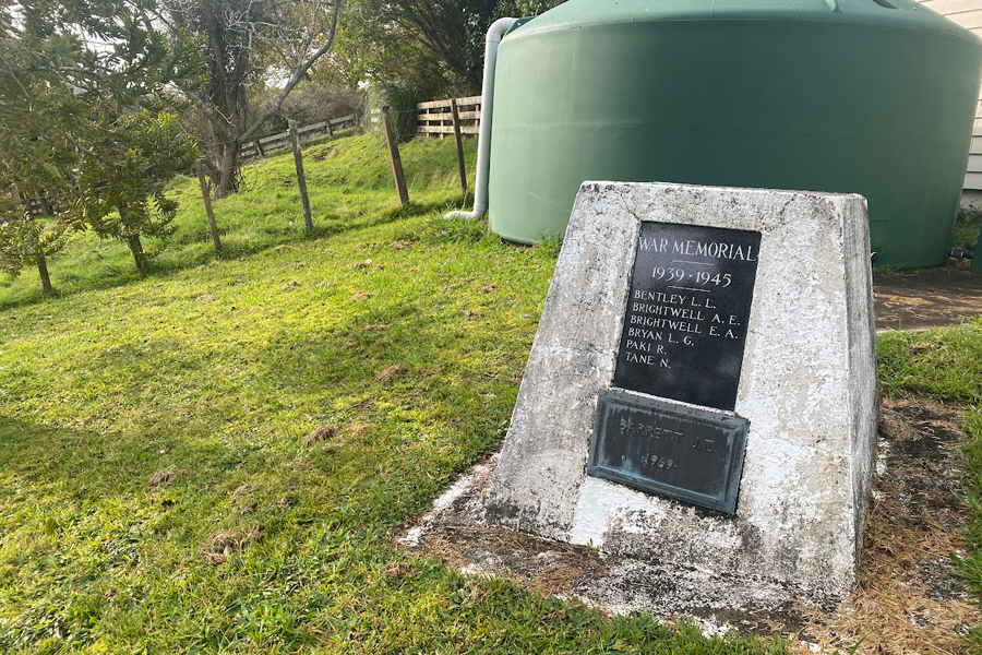 Concrete obelisk set into grass bank with green water tank in the background