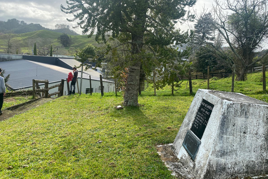 Concrete obelisk set into grass bank with trees, school buildings and rolling green hills in the background