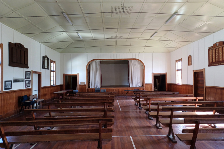 Rows of seats inside building with plaques attached to both walls and small stage in the background