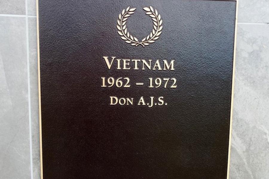 Square bronze plaque with a name in gold under picture of a laurel wreath and heading Vietnam 1962-1972